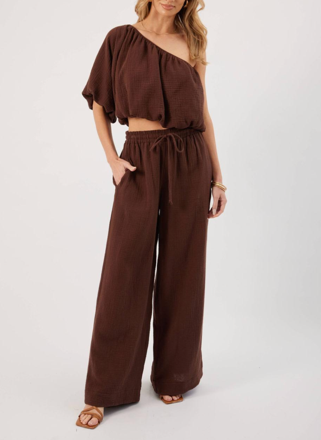 Model wearing brown KP Lina Top with one shoulder detail and bubble hem along with matching pants.