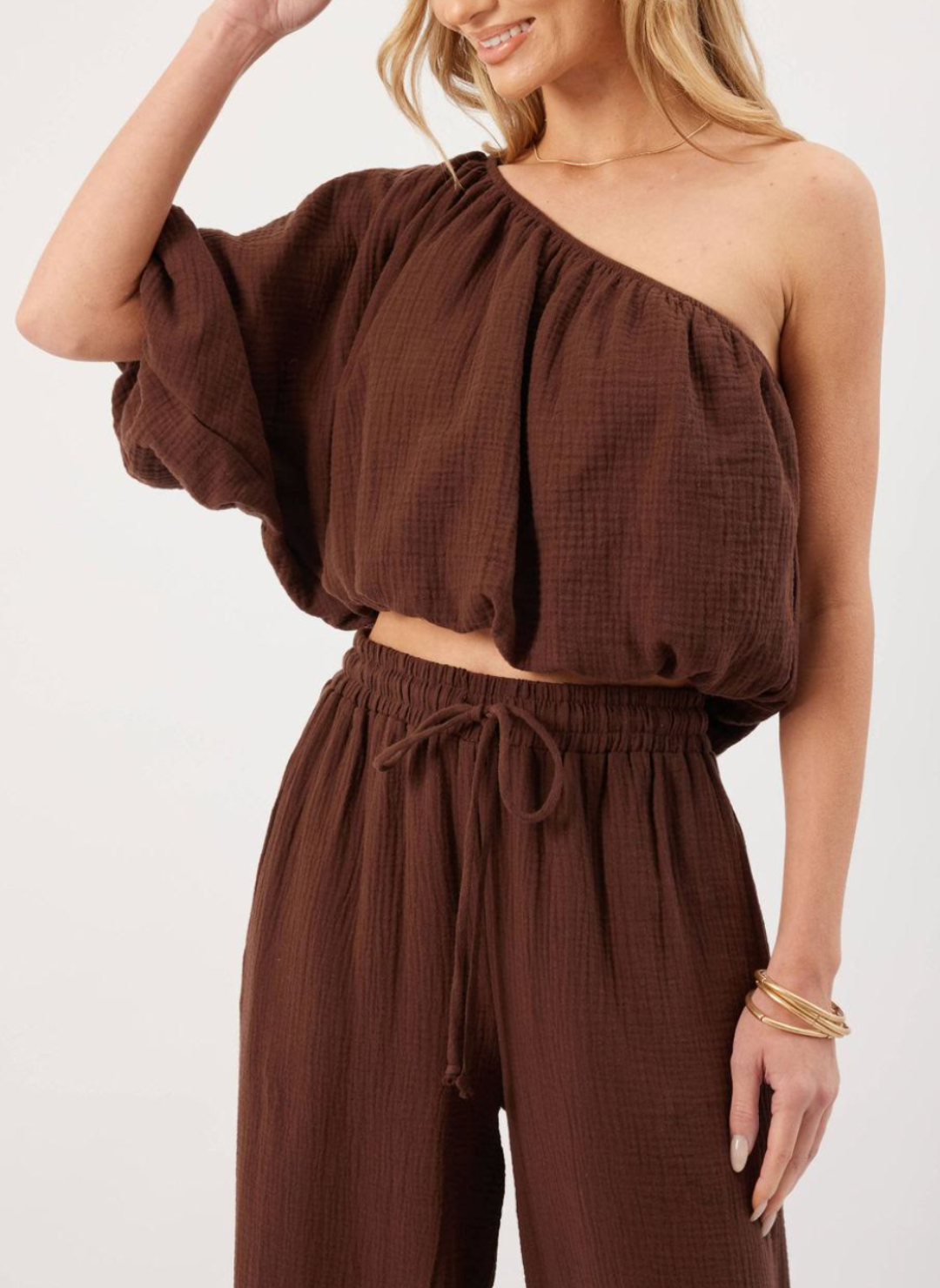  Model wearing brown KP Lina Top with one shoulder detail and bubble hem along with matching pants.