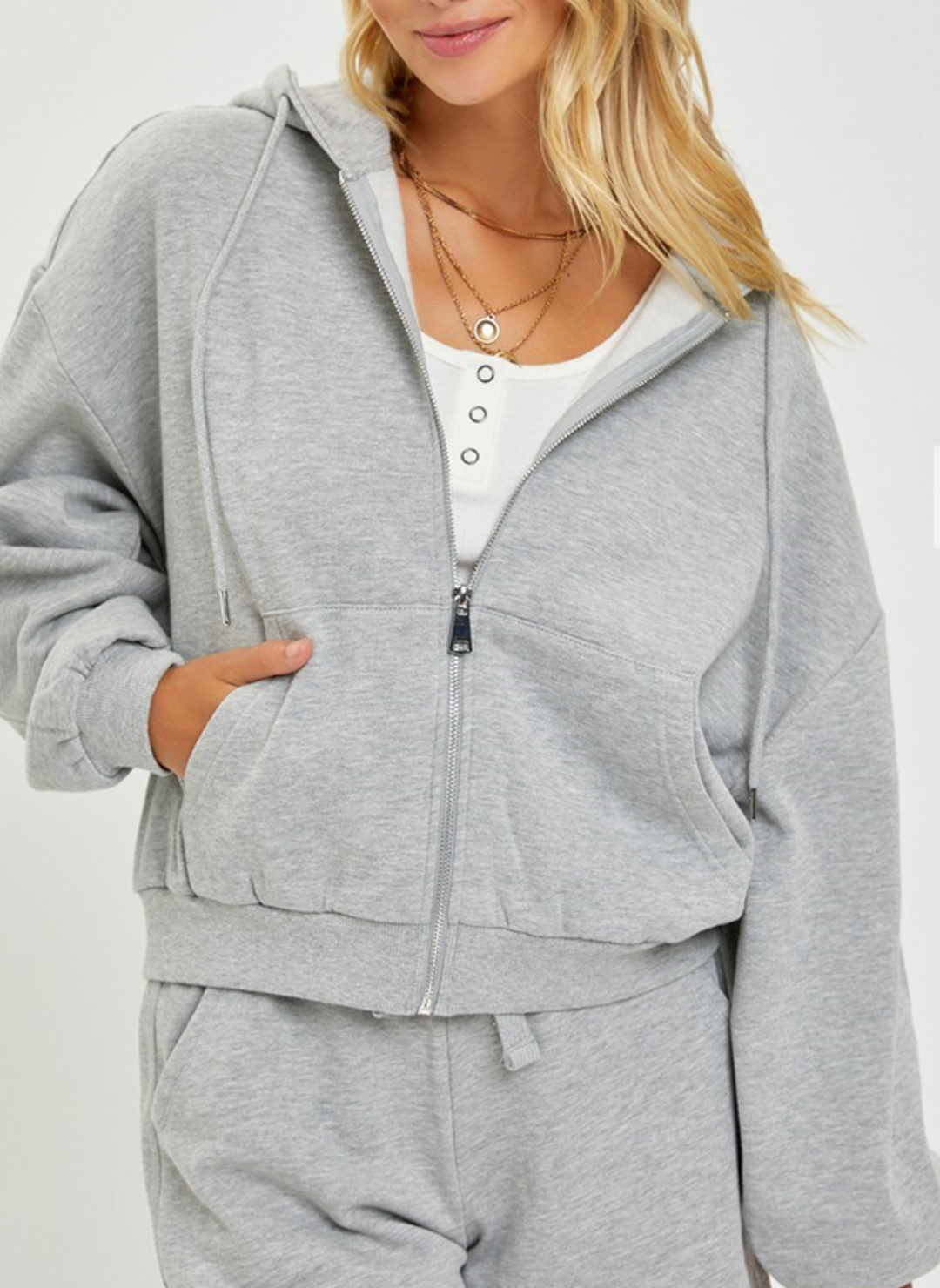 Front view of the model wearing the Risen Oversized Hoodie showing the zipper closure. Then showing that the hoodie has pockets by having her hand in the front pocket.