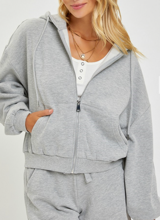 Front view of the model wearing the Risen Oversized Hoodie showing the zipper closure. Then showing that the hoodie has pockets by having her hand in the front pocket.