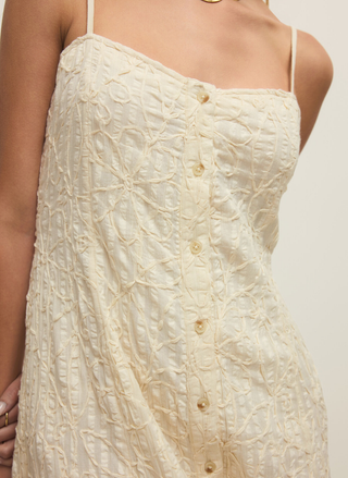 Close-up of a textured beige dress with button details on a plain background
