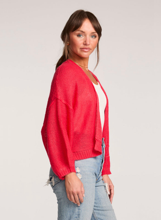 Woman wearing a red cardigan over a white shirt with light blue jeans on a plain background