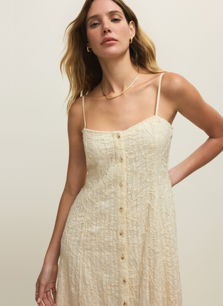 Woman wearing a beige dress with thin straps against a plain background