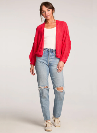 Woman wearing a red jacket, white top, and ripped jeans on a plain background