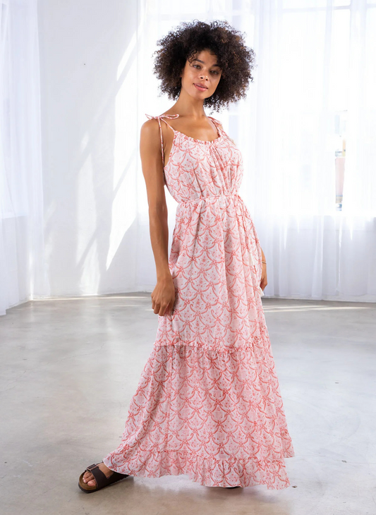 Woman wearing a pink and white printed maxi dress with tie straps, drawstring waist, and ruffle hem—breezy and lightweight, perfect for summer vacations or casual coastal days.