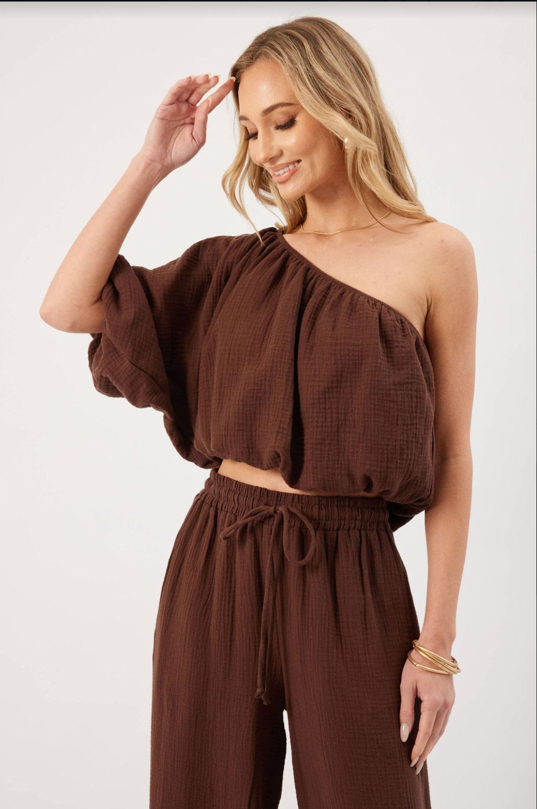  Model wearing brown KP Lina Top with one shoulder detail and bubble hem along with matching pants.