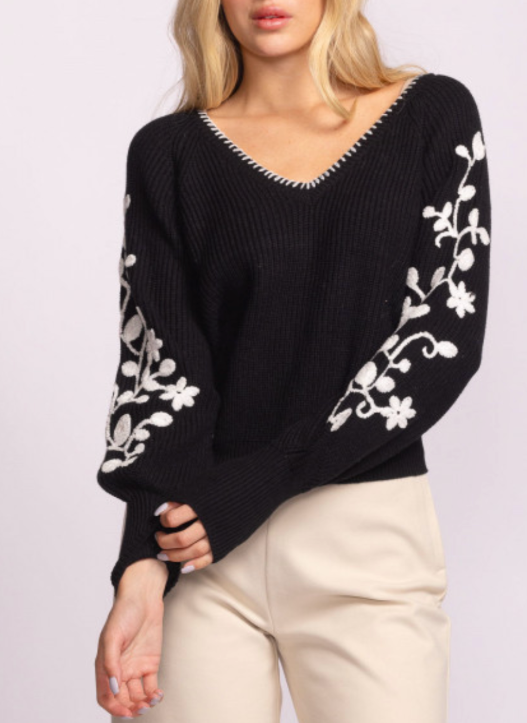 Woman wearing the Moonflower Sweater by Pink Martini, a black knit sweater with white floral embroidery on the sleeves, a V-neckline with whipstitch detail, and balloon sleeves. Boutique-style fall fashion with romantic, feminine details.