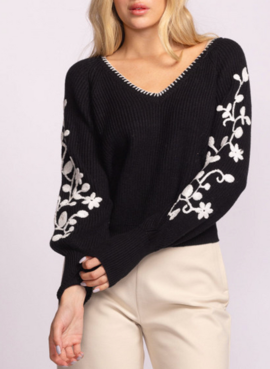 Woman wearing the Moonflower Sweater by Pink Martini, a black knit sweater with white floral embroidery on the sleeves, a V-neckline with whipstitch detail, and balloon sleeves. Boutique-style fall fashion with romantic, feminine details.