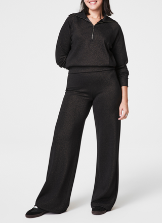 Full front view of pants with subtle sparkle standing in front of white background wearing black slippers. Model also wearing a matching top.