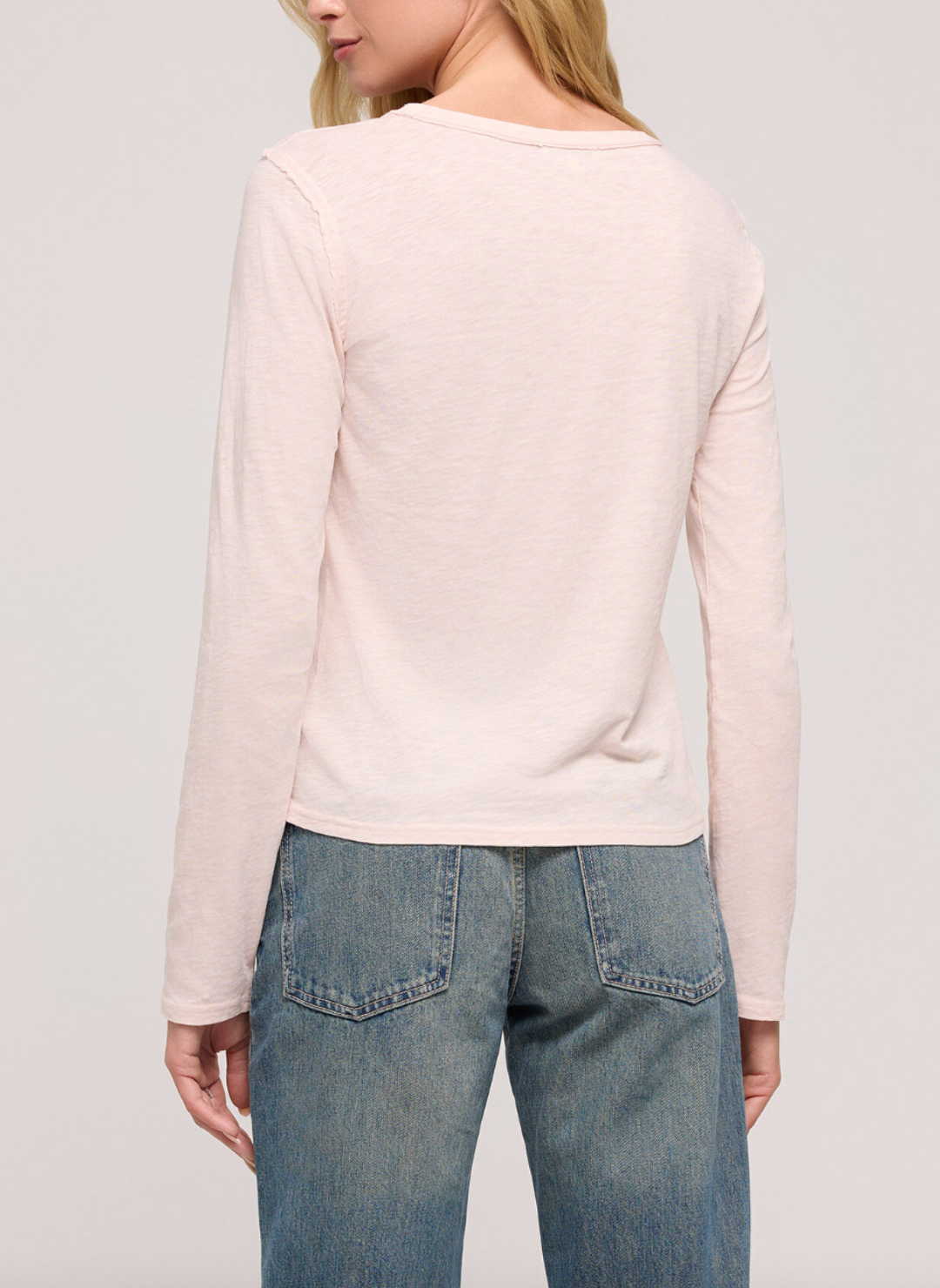 Back view of model wearing light pink long sleeve shirt with denim jeans.