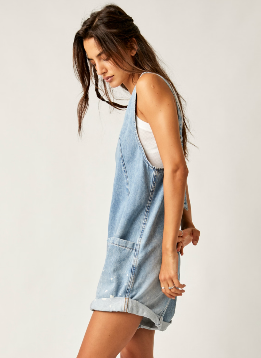 Model turned to the side wearing denim short romper that cuffs at the bottom. The side pockets are displayed in this view. 