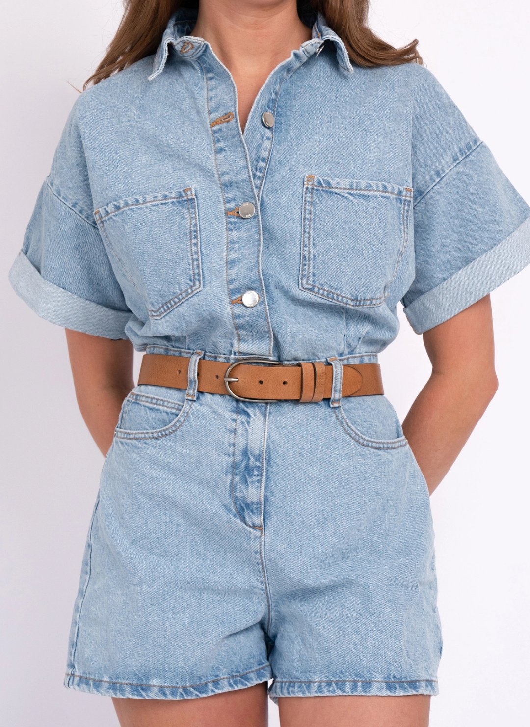 Model is wearing tan belt with denim romper. Models hands are behind her back displaying the belt. White background.