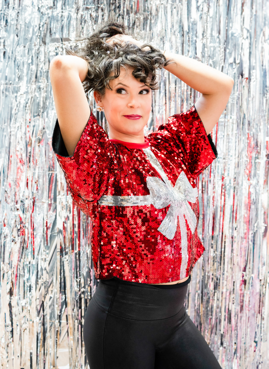 Model is playing with her hair while showing off the red sequin present top!