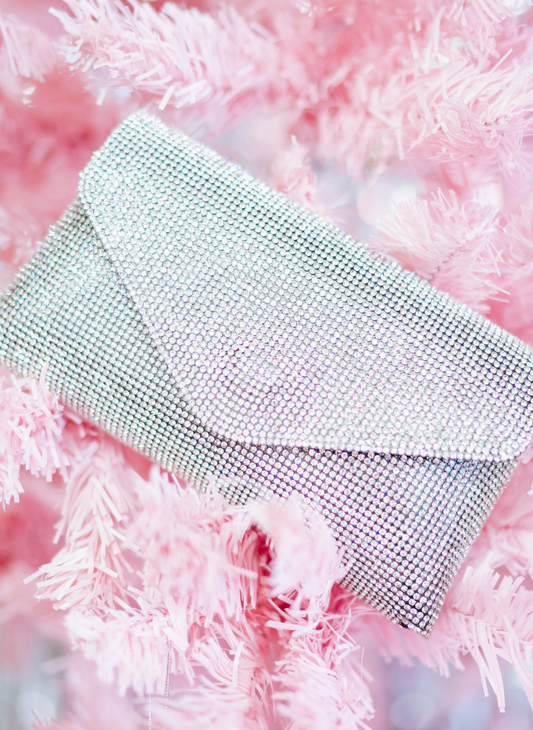 Image shows a silver shimmer clutch purse, layer on a pink fuzzy rug.