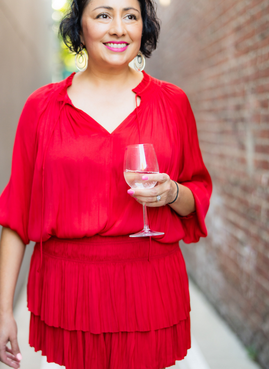 Model is posed with a glass of wine in her hand showing off the v neck of the cherry red dress.