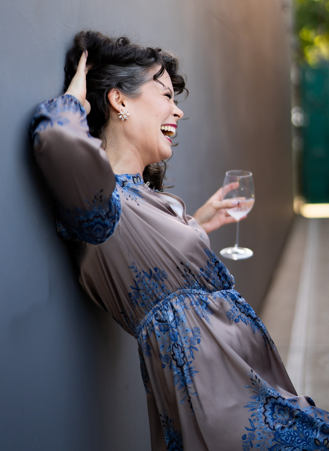 Model wearing Elinore Long Sleeve Dress
holding a glass of water. Model is leaning against a wall outside. 