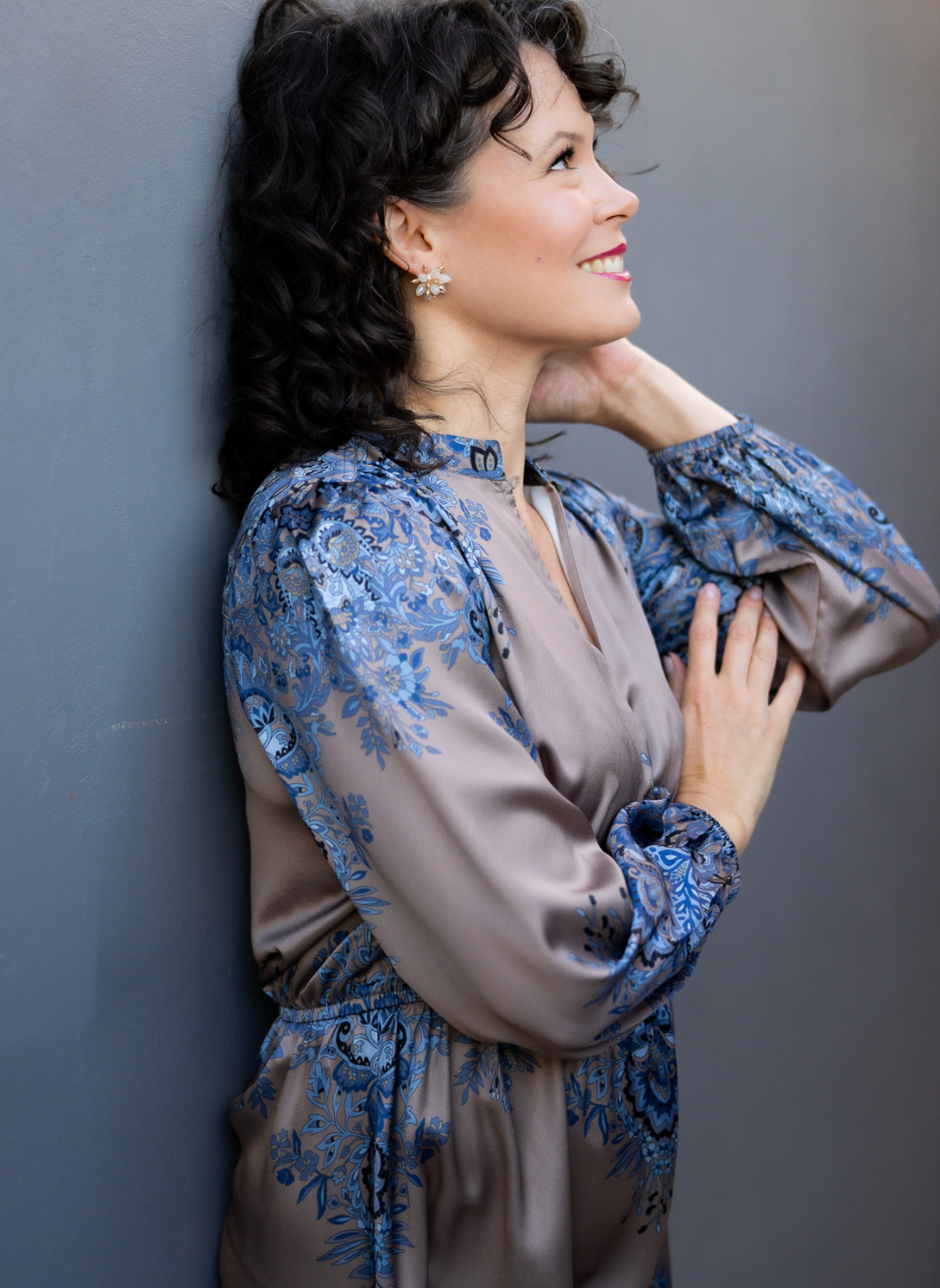 Full side view of model wearing the Elinore Long Sleeve Dress leaning against a wall outside.