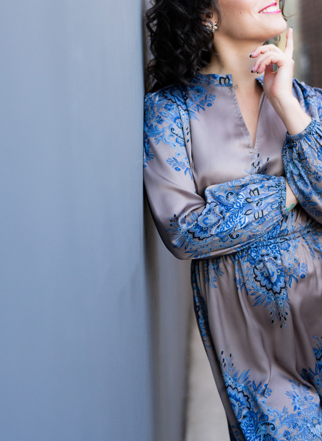 Full front view of model wearing the Elinore Long Sleeve Dress leaning against a wall outside.