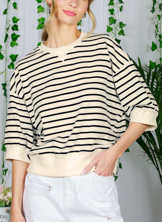 Full front view of model wearing Katie Striped Crew Top paired with white pants. Model is standing in front of greenery arrangement.