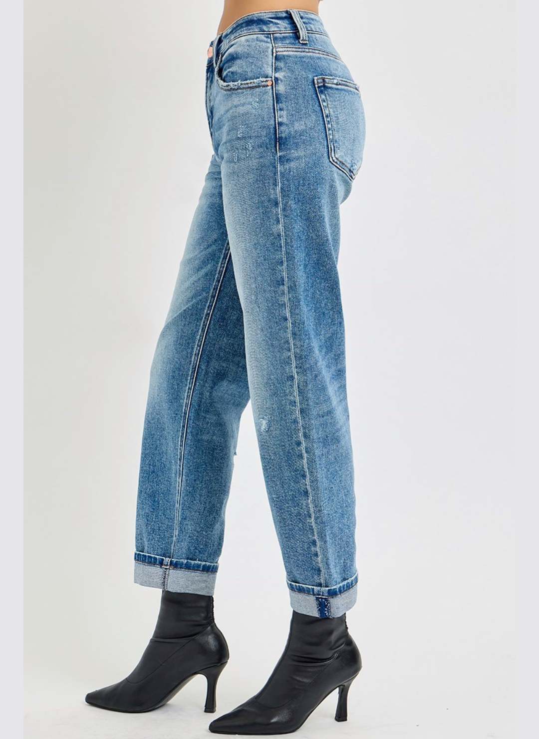 Side view of distressed denim jeans with back leg slightly out in-front of the other leg. These are paired with black ankle boots.