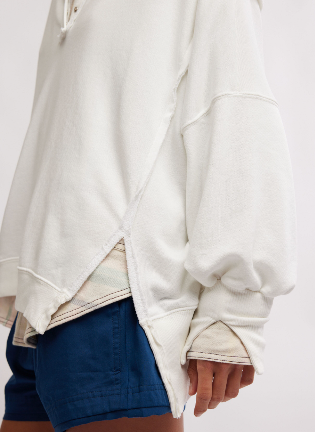 Model is turned to the side wearing white Camden pullover sweatshirt displaying the small slit at the bottom of the sweatshirt.