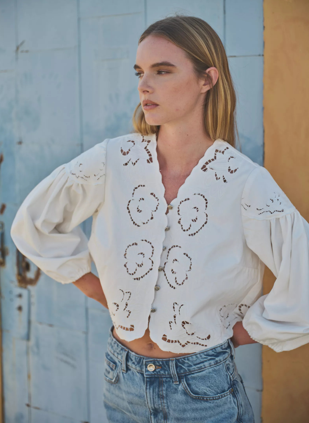 Model is wearing embroidered cream colored blouse. Models hands and on hips displaying the flowy styled sleeve.