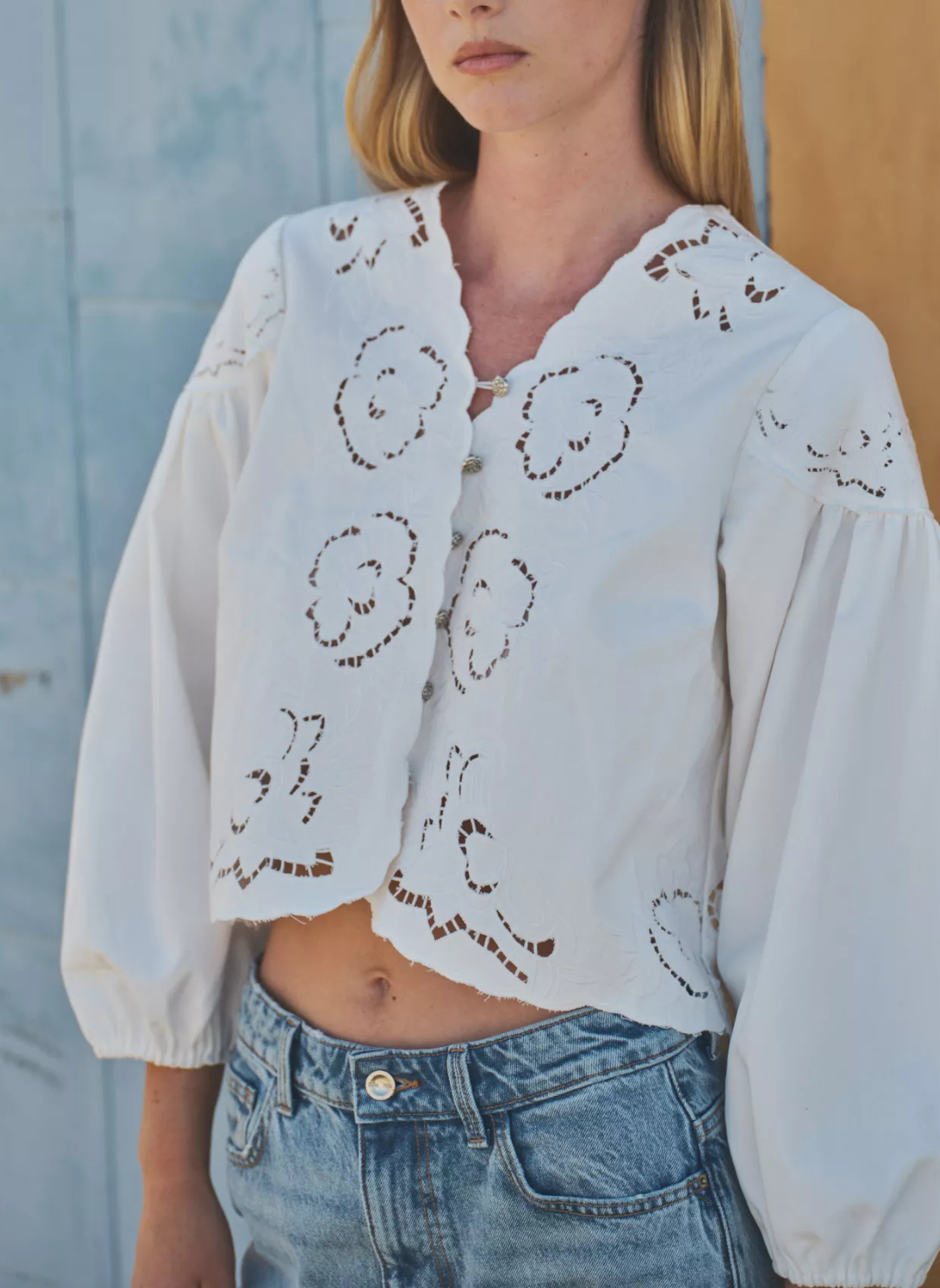 Close up view of embroidered detail in cream colored blouse and scalloped neckline. 