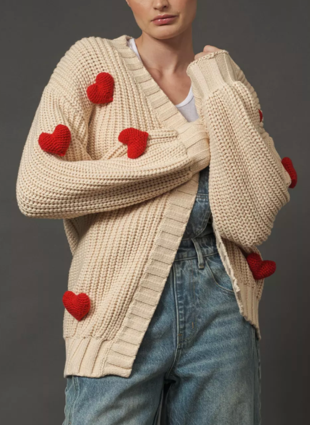 Model is wearing cream colored sweater with puffy red hearts. Models arms are in front of her showing off the hearts on the sweater.