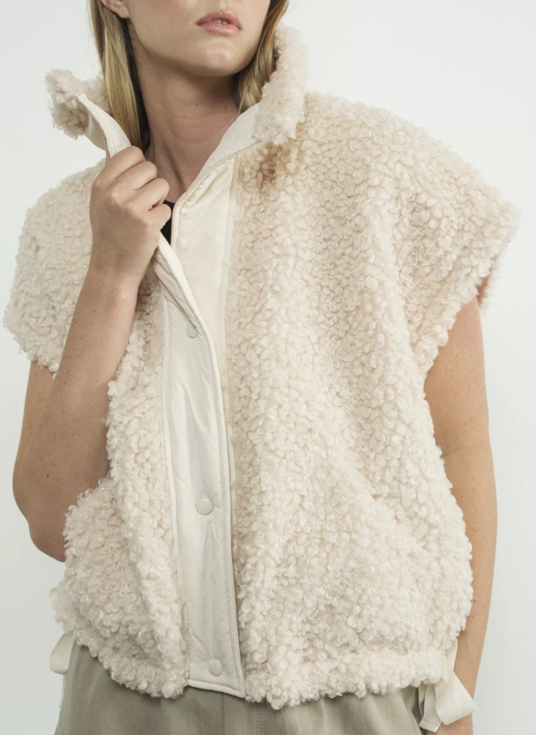 Front view of snow colored fuzzy button down vest. Models left hand is at the collar of the vest and other hand is by her side. 