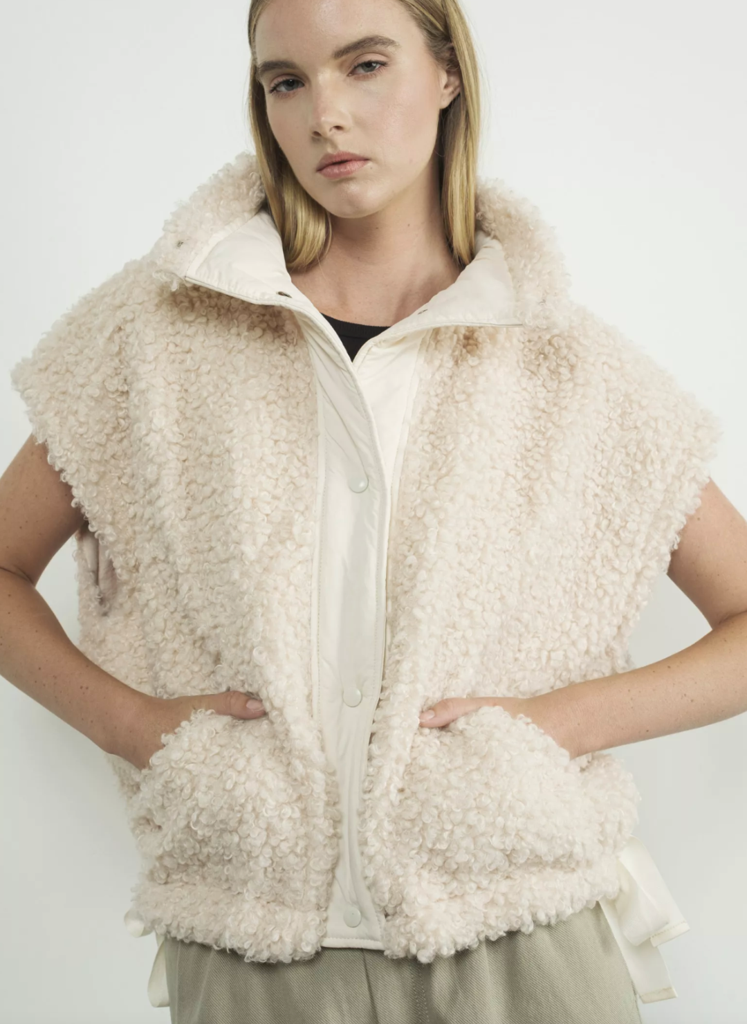 Front view of snow colored fuzzy buttoned up vest. Models hands are in front pockets. White background. 