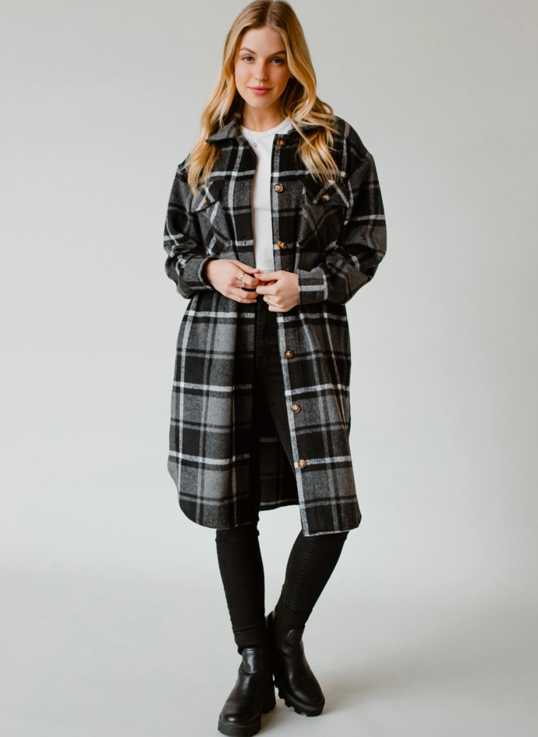 Model is posing with arms in front of body wearing longer length black and white Pricilla Plaid Shacket. The coat has brown buttons down the front. Model is also Wearing black pants and a white shirt underneath the shacket. 