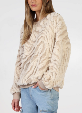 Model is wearing tan and cream sweater. Models right hand is in pocket, portraying a closer view of the sweaters textured detail.