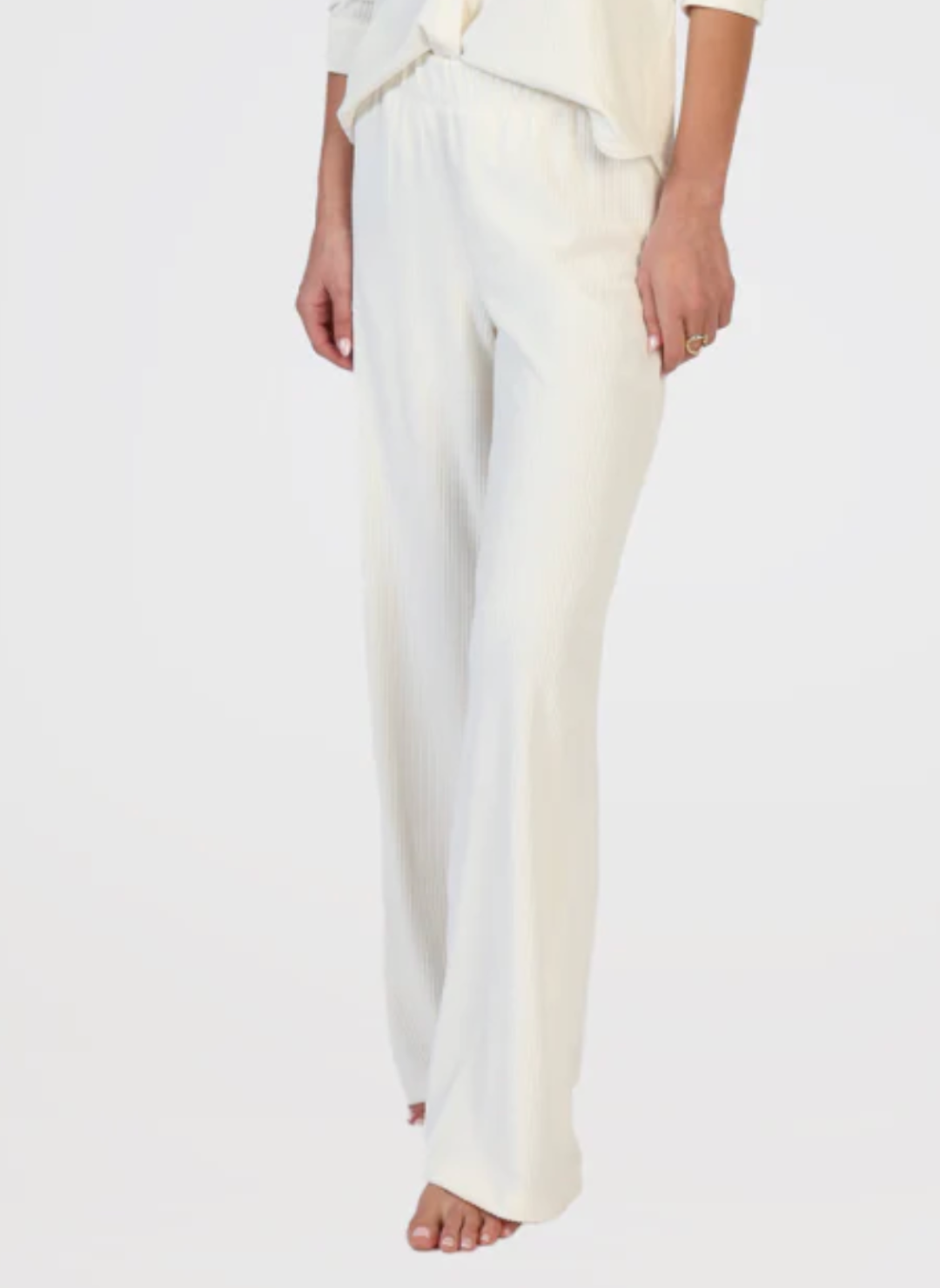 Model is wearing white ribbed pants with arms by side. White background.