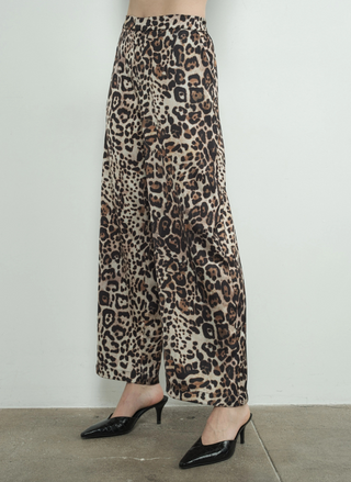 Side view of model wearing the Dangerously Leopard Satin Pants paired with black heels. Model is standing infringe of a white background.