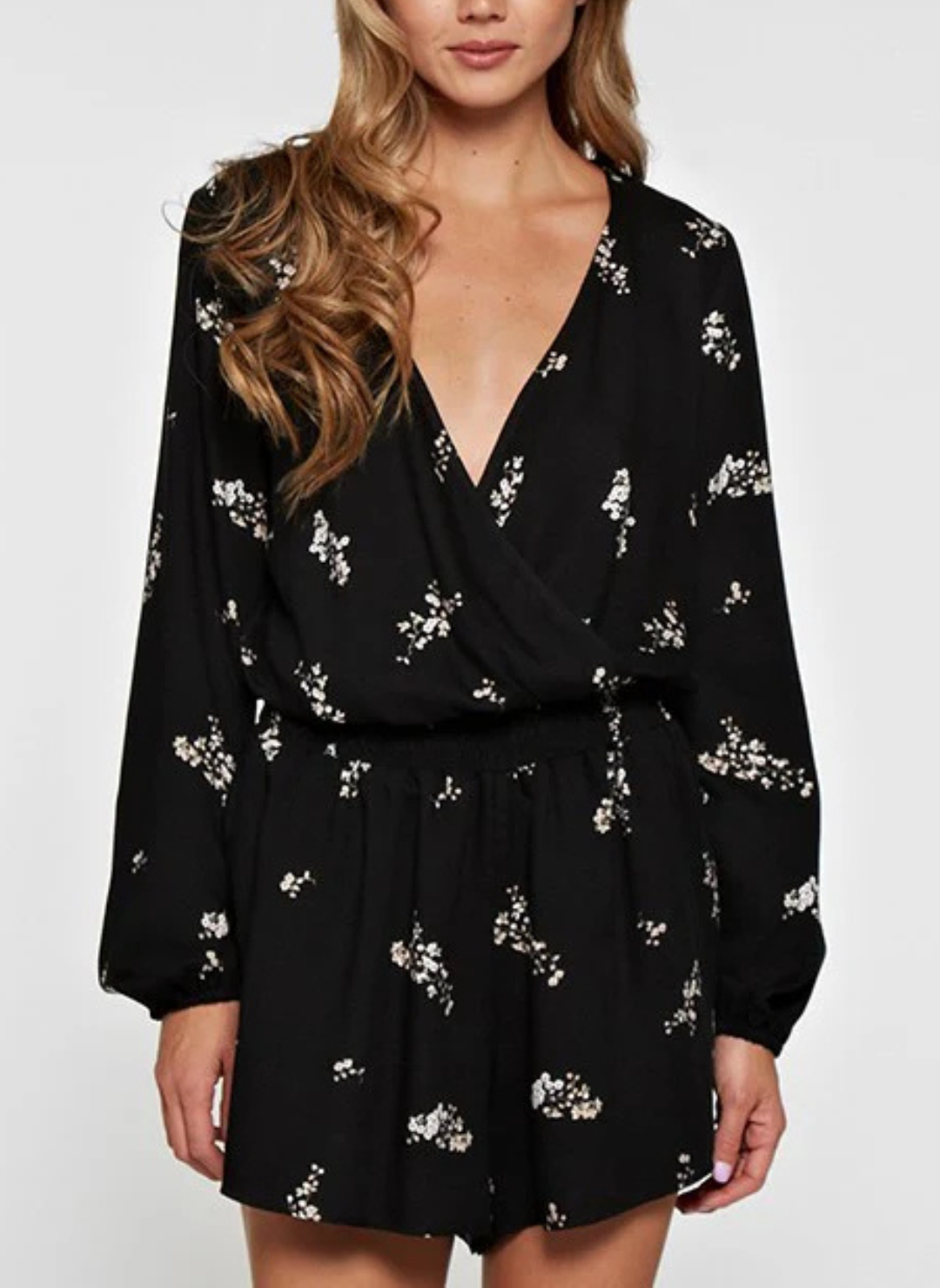 Woman wearing a black floral romper with long sleeves, surplice wrap front, and elastic waist—lightweight, flattering, and perfect for spring events, date nights, or travel.
