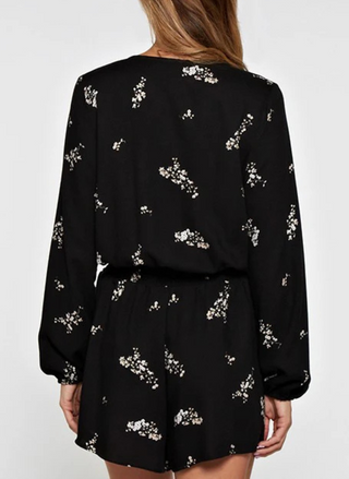 Back view of a woman wearing a black floral romper with long sleeves, surplice wrap front, and elastic waist—lightweight, flattering, and perfect for spring events, date nights, or travel.