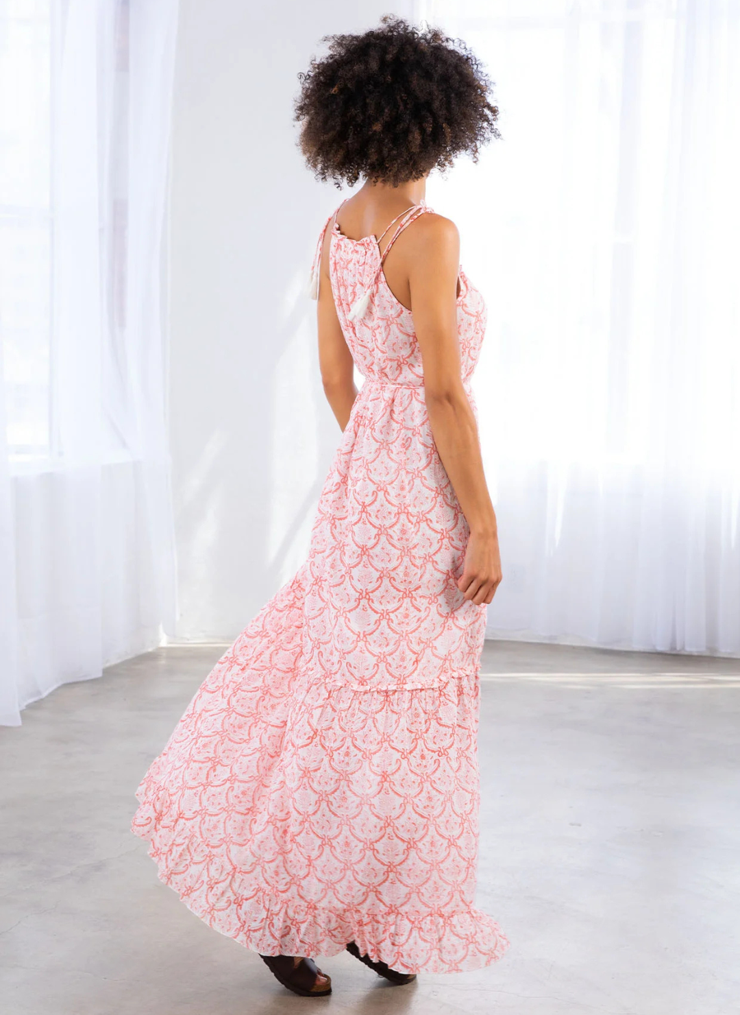 Woman wearing a pink and white printed maxi dress with tie straps, drawstring waist, and ruffle hem—breezy and lightweight, perfect for summer vacations or casual coastal days.