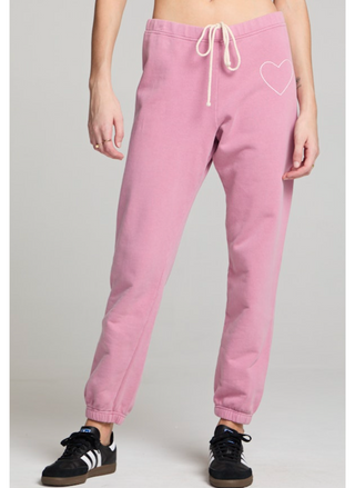 Woman wearing blush pink jogger sweatpants with white heart detail at the hip and elastic ankle cuffs. 