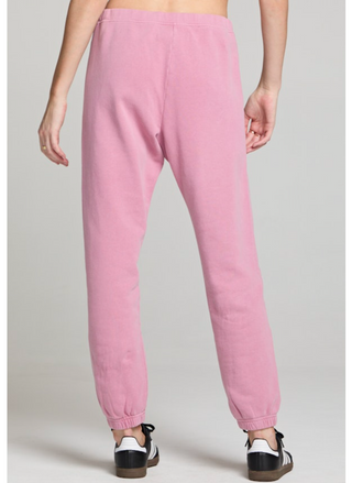 Back view of a woman wearing blush pink jogger sweatpants with white heart detail at the hip and elastic ankle cuffs. 