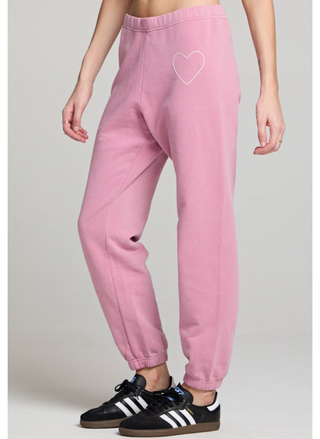 Woman wearing blush pink jogger sweatpants with white heart detail at the hip and elastic ankle cuffs.