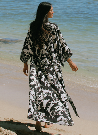Woman standing in front of the ocean wearing a printed kimono over a black-and-white polka dot swimsuit.