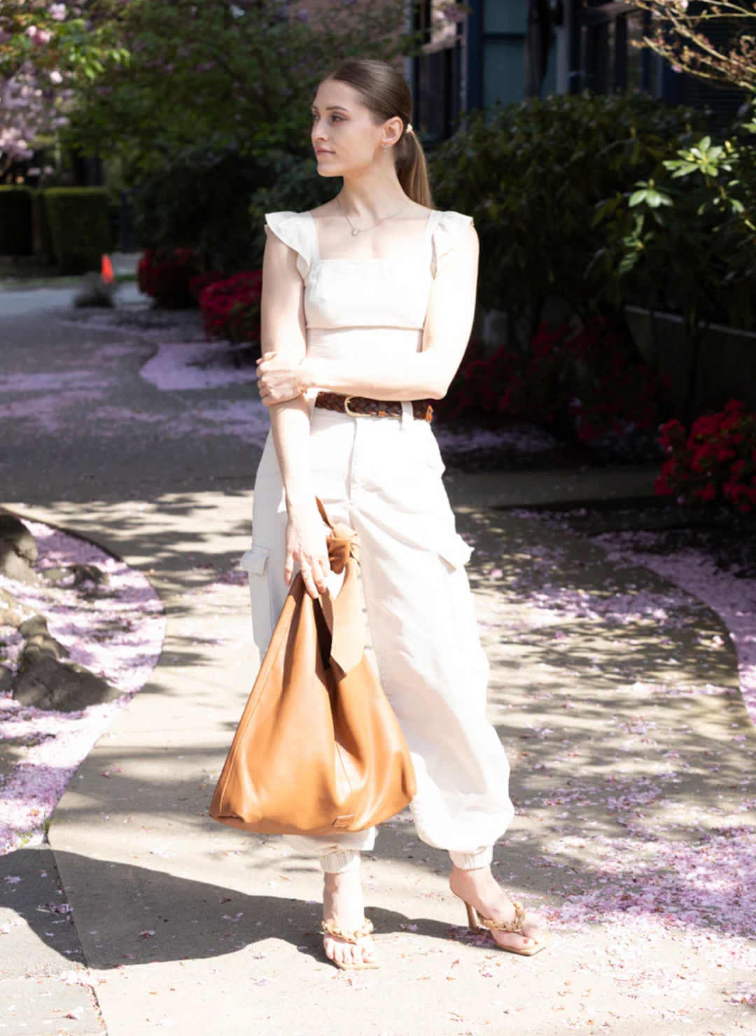 Woman holding flowers and wearing a stylish, large caramel-colored suede RISA upcycled handbag. The handcrafted shoulder bag complements her chic outfit, ideal for sustainable fashion lovers.