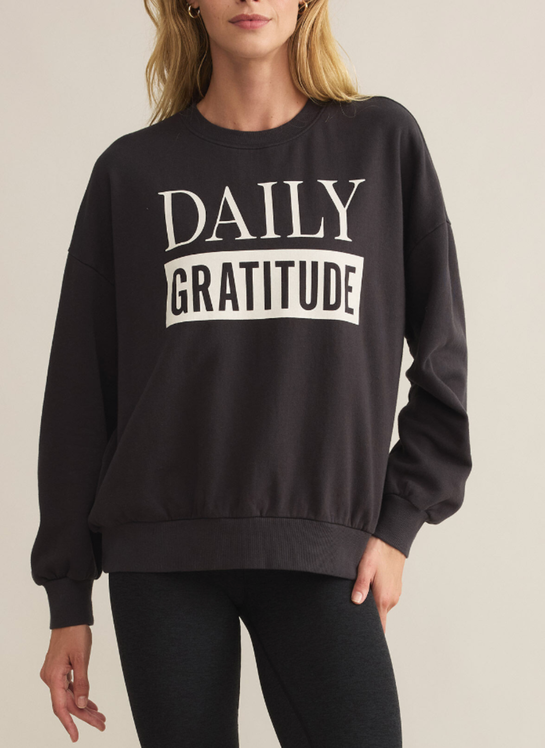 Model is wearing a dark gray crew neck with white lettering that spells out “Daily Gratitude”