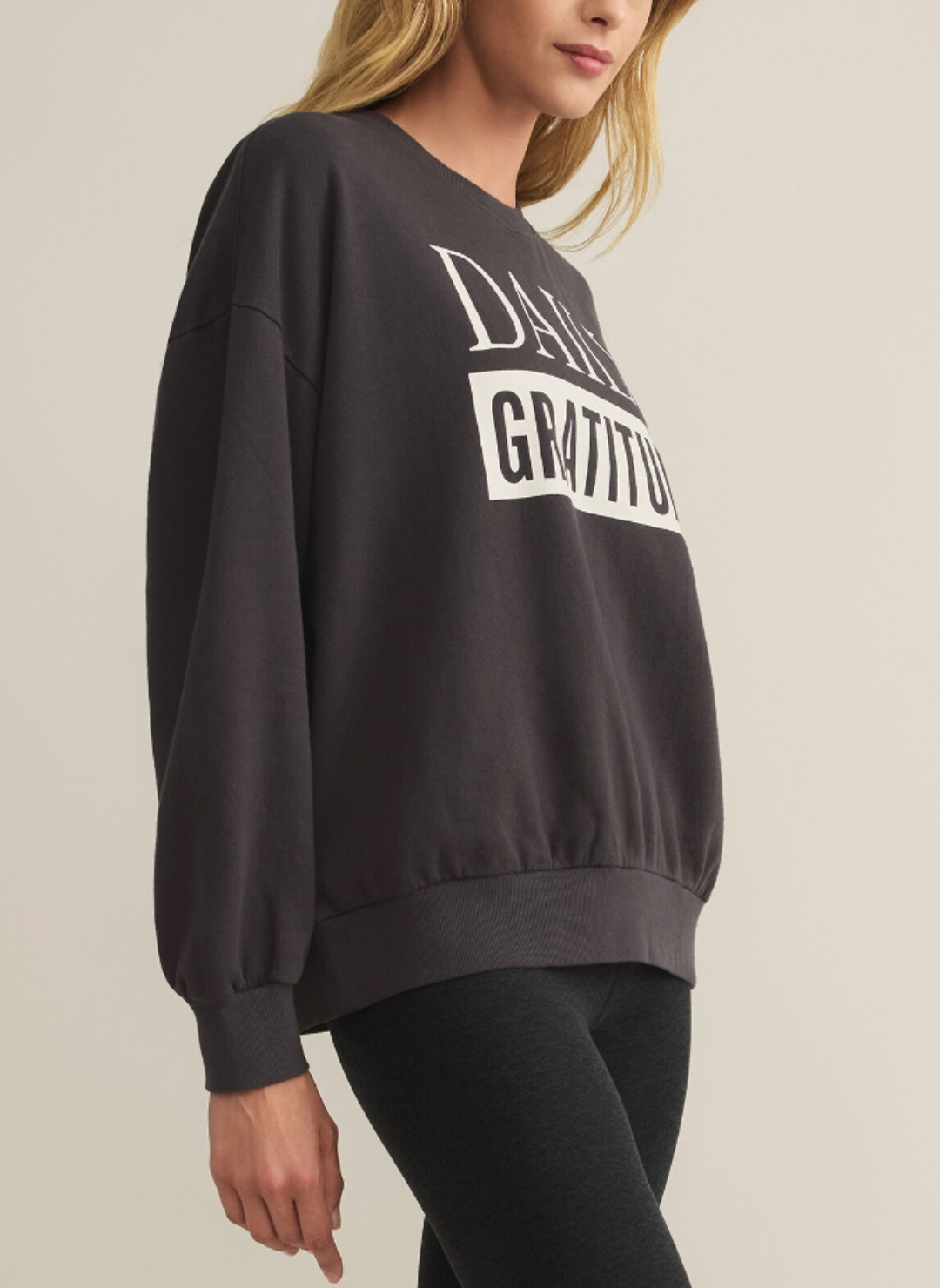 Model is wearing a gray crew neck that spells out “Daily Gratitude” 