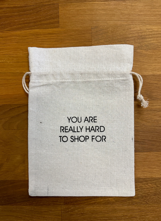 Image shows a small bag that says “you are really hard to shop for” with a string drawcord.