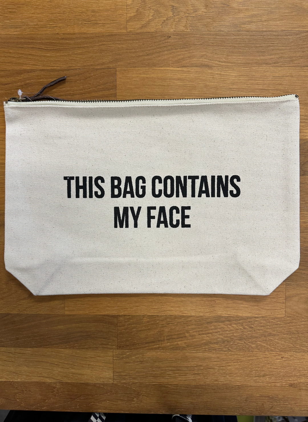 Image shows a makeup bag with a zipper, bag states “this bag contains my face”