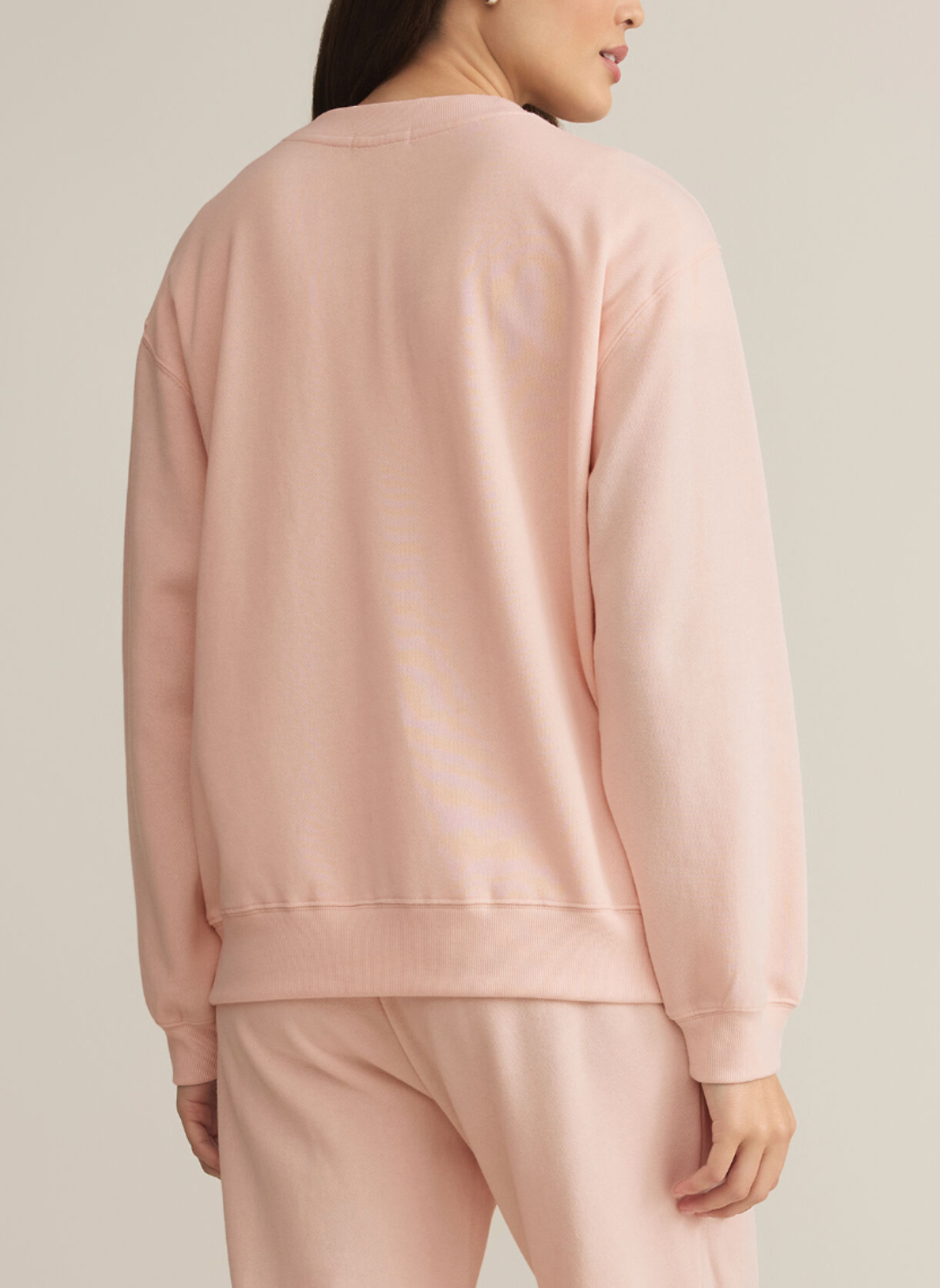 Model is wearing pink Boyfriends sweatshirt. Is turned around showing the back of the sweatshirt.