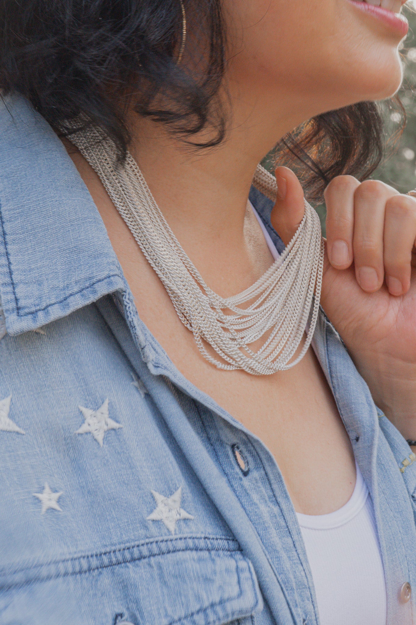 Side view of the model wearing the Ocean Waves Chain Necklace. Color is silver. Model is holding the necklace