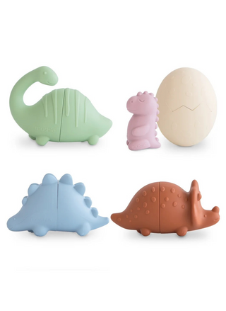 Mushie Dino Mold Free Bath Play Set 4 Pack featuring colorful dinosaur-shaped silicone bath toys in green, purple, blue, and brown with a cream cracked dinosaur egg