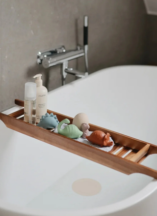 Mushie Dino Mold Free Bath Play Set being used beside a modern bathtub, showing colorful silicone dinosaur toys designed for imaginative bath time play